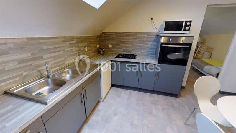 Cuisine moderne sous combles avec évier double, plaques de cuisson, four, micro-ondes et mobilier gris.