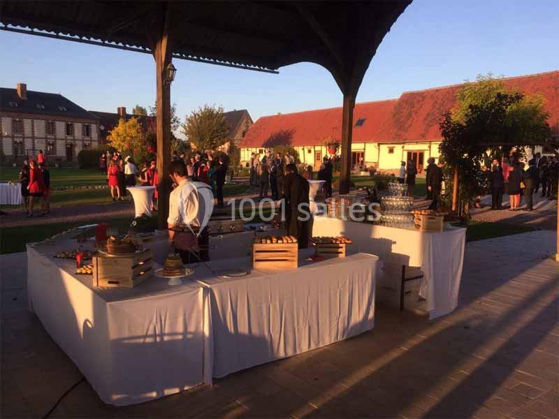 Tables de buffet dressées sous un auvent, avec des invités en arrière-plan dans une cour au coucher du soleil.