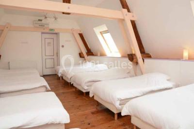 Salle de bain moderne avec douche vitrée, lavabo blanc, miroir, sèche-serviettes et poutres en bois apparentes.