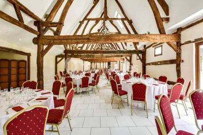 Salle de bain moderne avec douche vitrée, lavabo blanc, miroir, sèche-serviettes et poutres en bois apparentes.