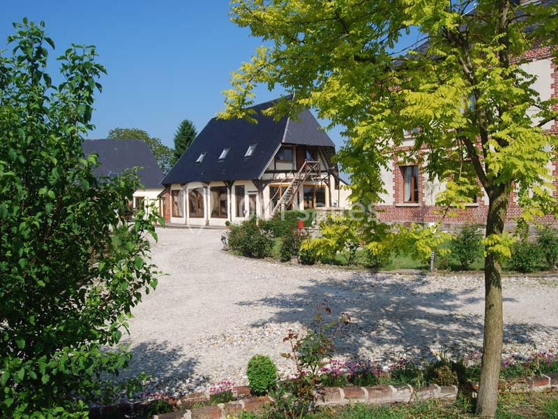 Cour d'une maison traditionnelle avec façade en briques et colombages, entourée d'arbres et de végétation.