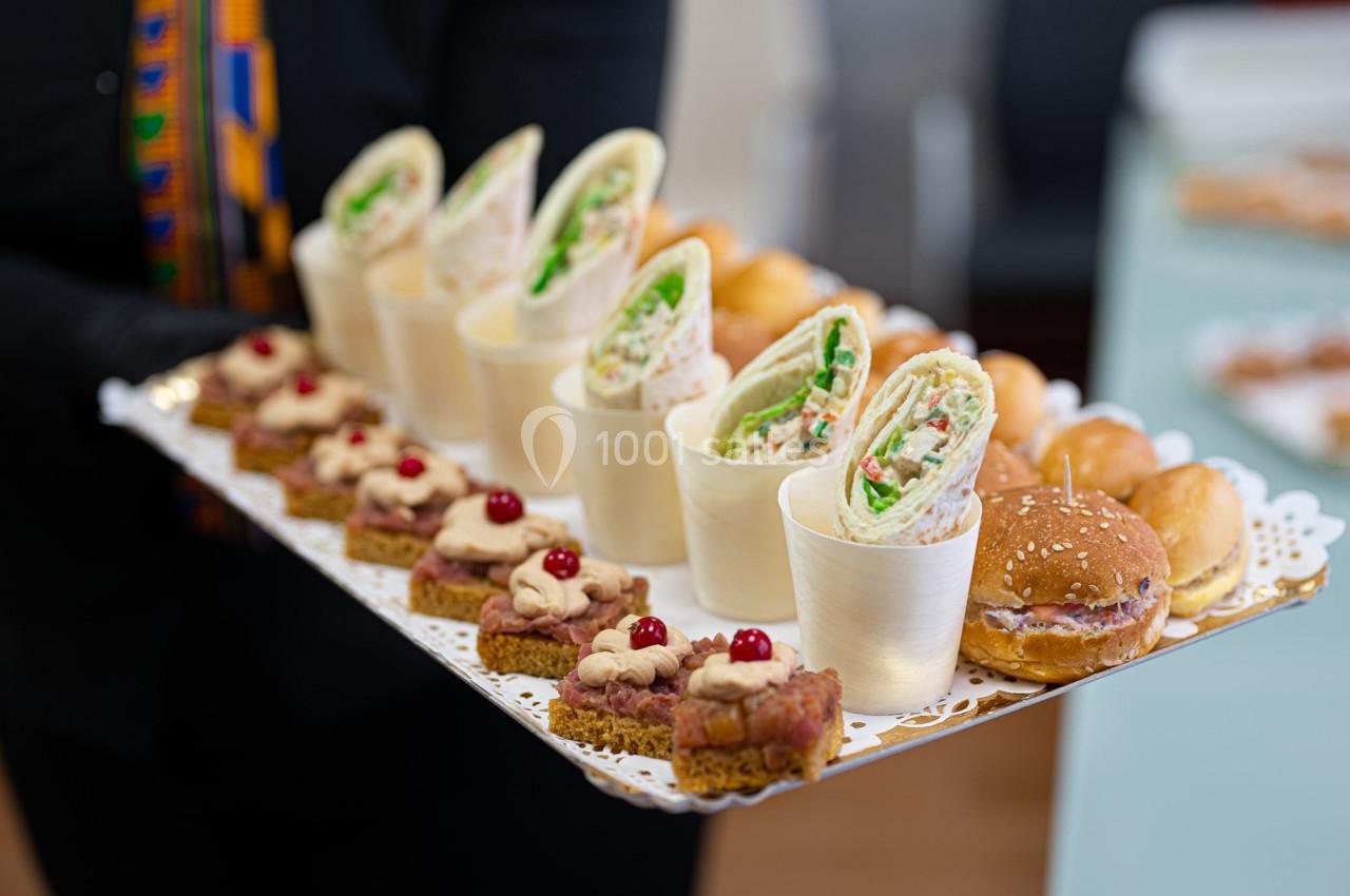 Plateau de bouchées variées comprenant wraps, mini-burgers et canapés décorés de baies rouges.