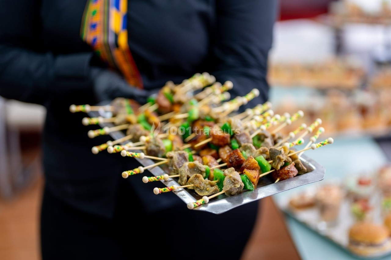 Un serveur présente un plateau de brochettes colorées composées de viande et de légumes lors d'un événement.