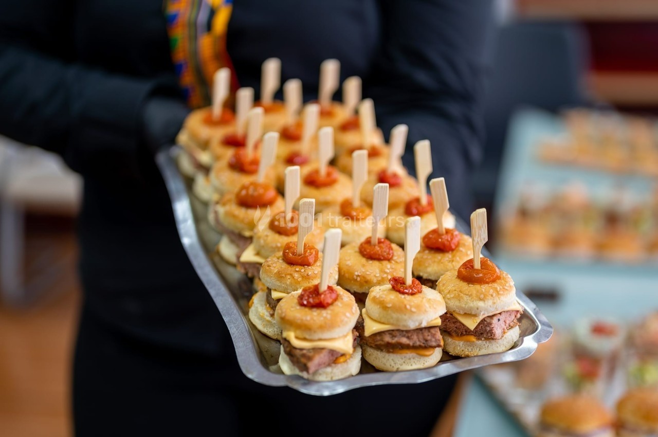 Plateau de mini-burgers garnis de fromage et de sauce, chacun maintenu par un pique en bois.