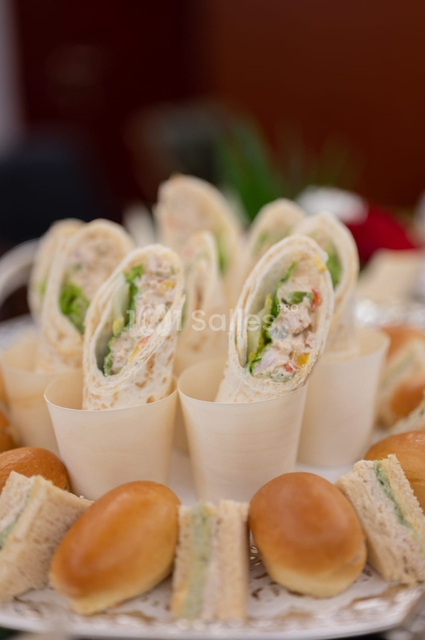 Assortiment de wraps garnis de légumes et de poulet, entourés de petits pains et de sandwichs sur un plateau.