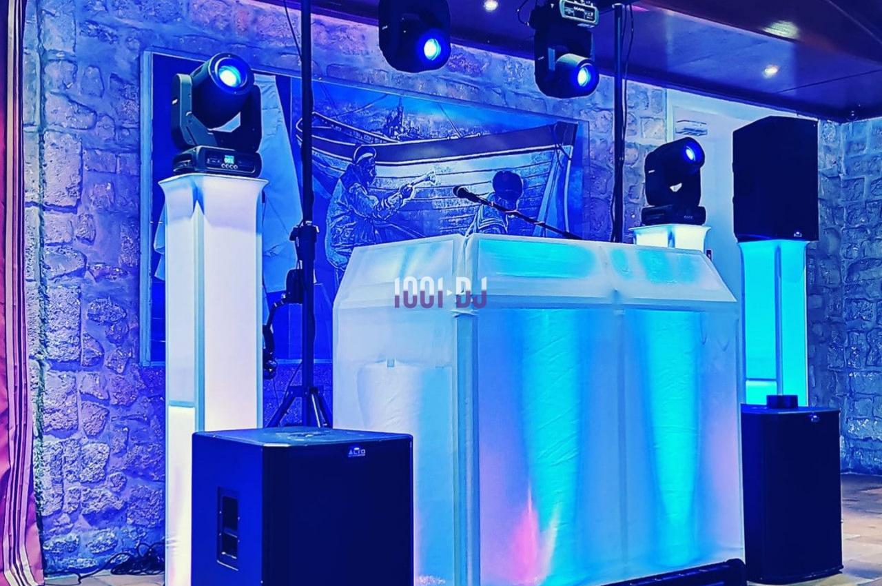 Installation de matériel de sonorisation et d'éclairage avec une table de DJ illuminée dans une salle en pierre.