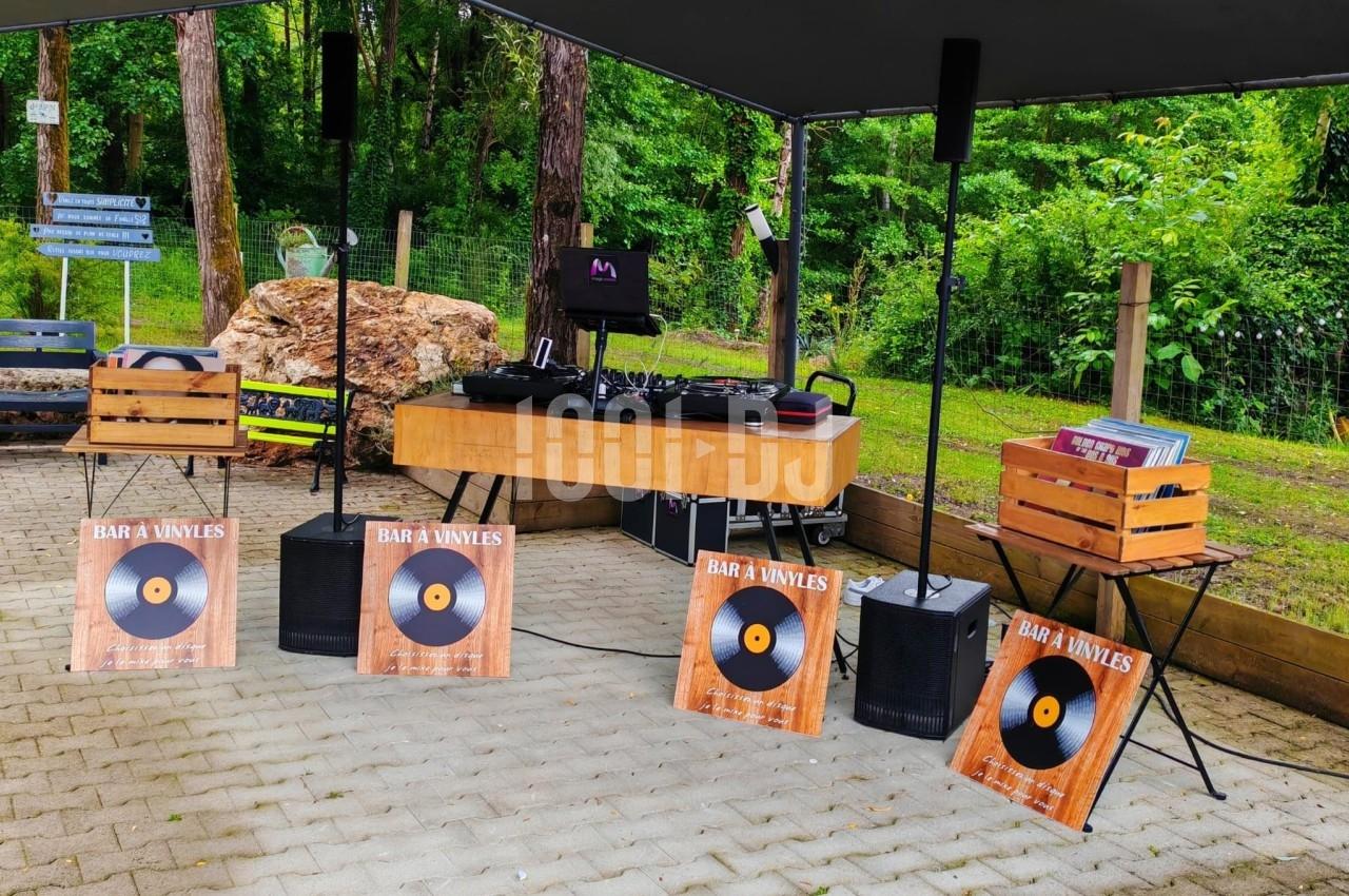 Stand de DJ en plein air avec platines vinyles, enceintes et caisses en bois, entouré de verdure.