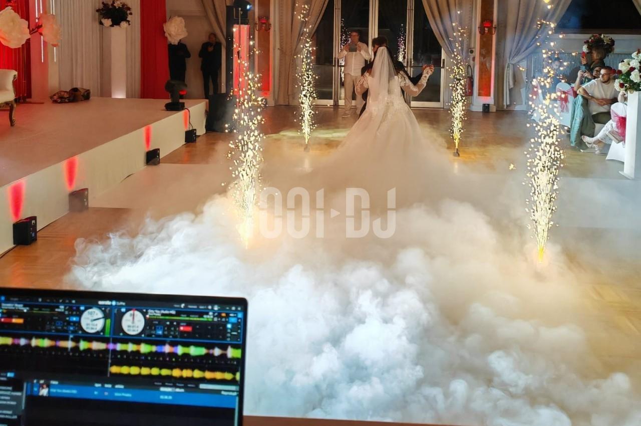 Un couple de mariés danse au milieu d'effets de fumée et d'étincelles dans une salle de réception décorée.