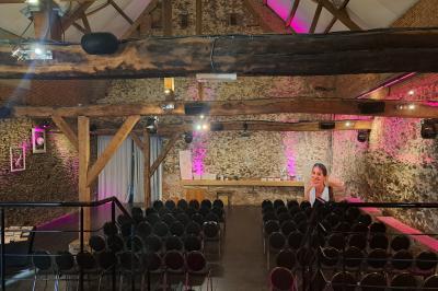 Salle lumineuse avec bar en bois, tables en verre, chaises noires et grandes fenêtres laissant entrer la lumière naturelle.