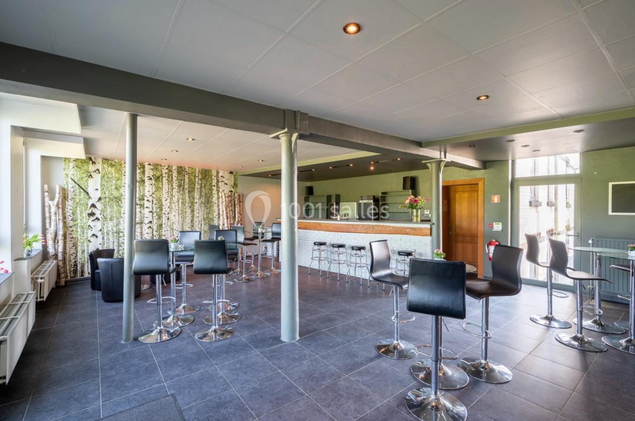 Salle moderne avec tables hautes, chaises noires et bar en bois clair, décorée de panneaux imitant des troncs de bouleaux.
