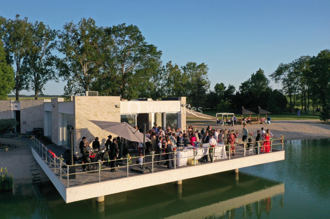 Groupe de personnes rassemblées sur une terrasse au bord d'un plan d'eau, entourée de verdure par temps ensoleillé.