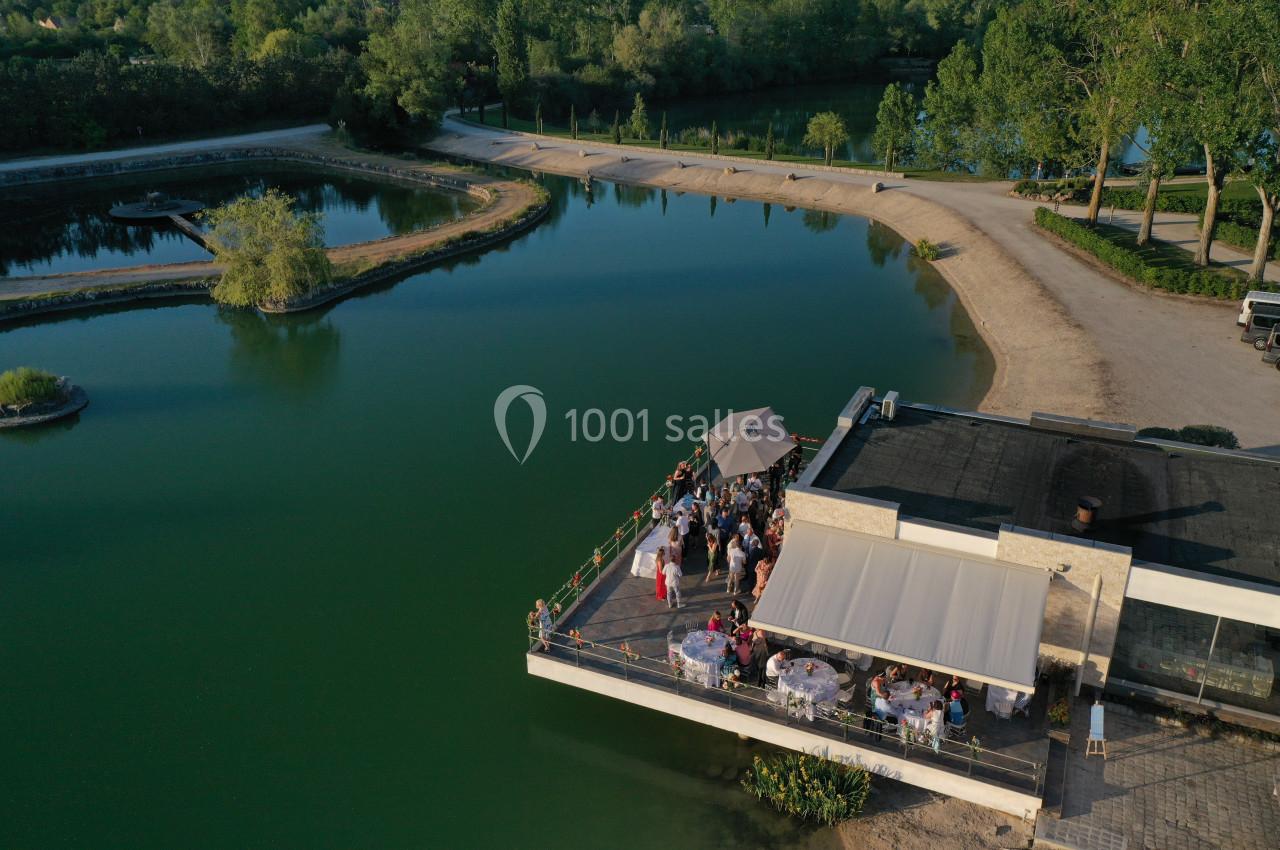 Terrasse d'un bâtiment au bord d'un lac, occupée par des convives lors d'un événement en plein air.
