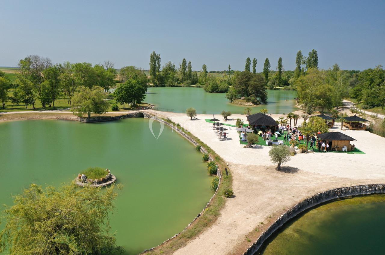 Vue aérienne d'un espace naturel avec des étangs, une petite île végétalisée et des structures en bois entourées de verdure.