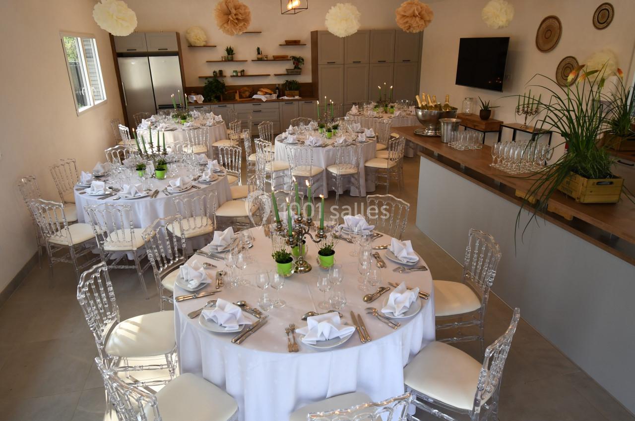 Salle décorée pour un événement avec tables rondes dressées, nappes blanches, chaises transparentes et décorations…