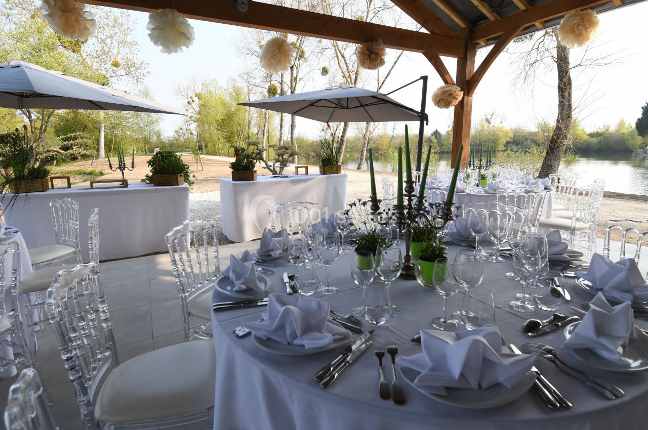 Tables rondes élégamment dressées sous une pergola en bois, avec vue sur un étang et une végétation verdoyante.