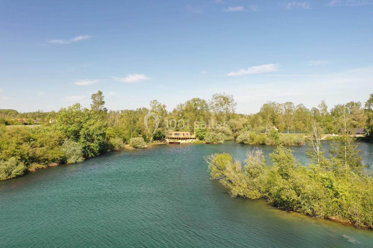 Vue aérienne d'un lac entouré de végétation dense avec une petite maison en bois au bord de l'eau.