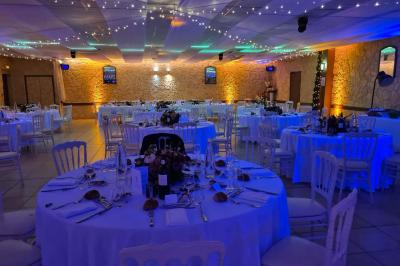 Salle vide avec un sol en parquet sombre, murs blancs, fenêtres et piliers gris sous un plafond à dalles blanches.