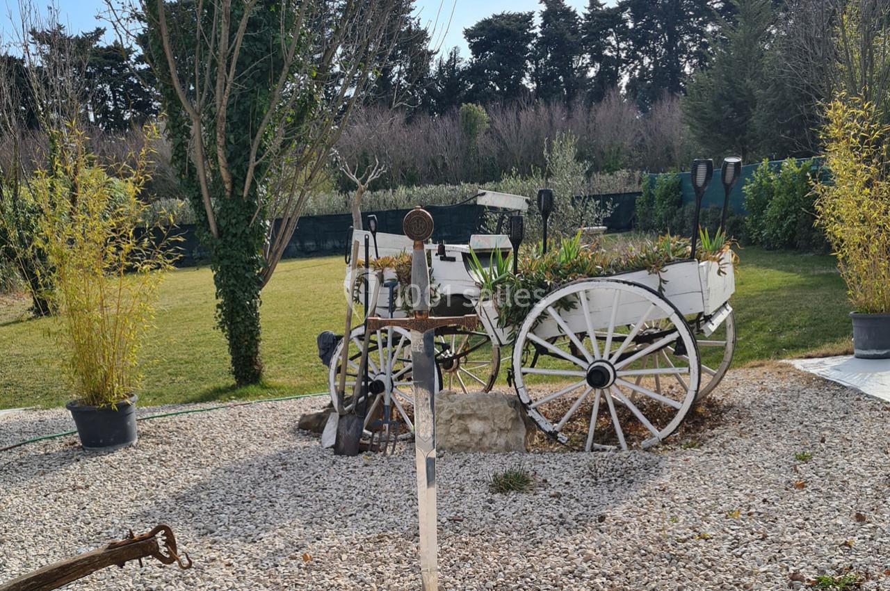 Charrette blanche ancienne décorative remplie de plantes, entourée de graviers et de végétation dans un jardin.