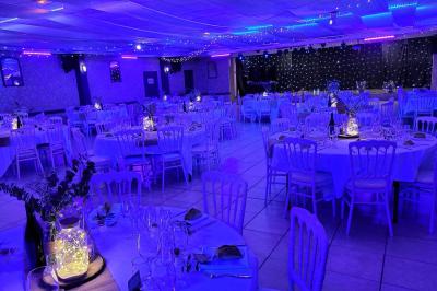 Salle vide avec un sol en parquet sombre, murs blancs, fenêtres et piliers gris sous un plafond à dalles blanches.