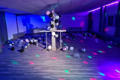 Salle vide avec un sol en parquet sombre, murs blancs, fenêtres et piliers gris sous un plafond à dalles blanches.