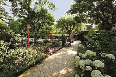 Deux chaises en bois et une table ronde avec un seau à glace sur une terrasse donnant sur un jardin verdoyant.