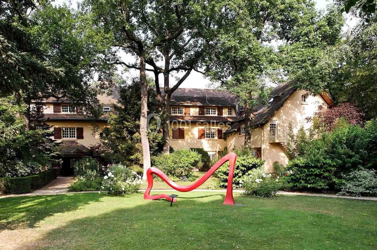 Jardin verdoyant avec une sculpture rouge moderne devant une grande maison à l'architecture traditionnelle.