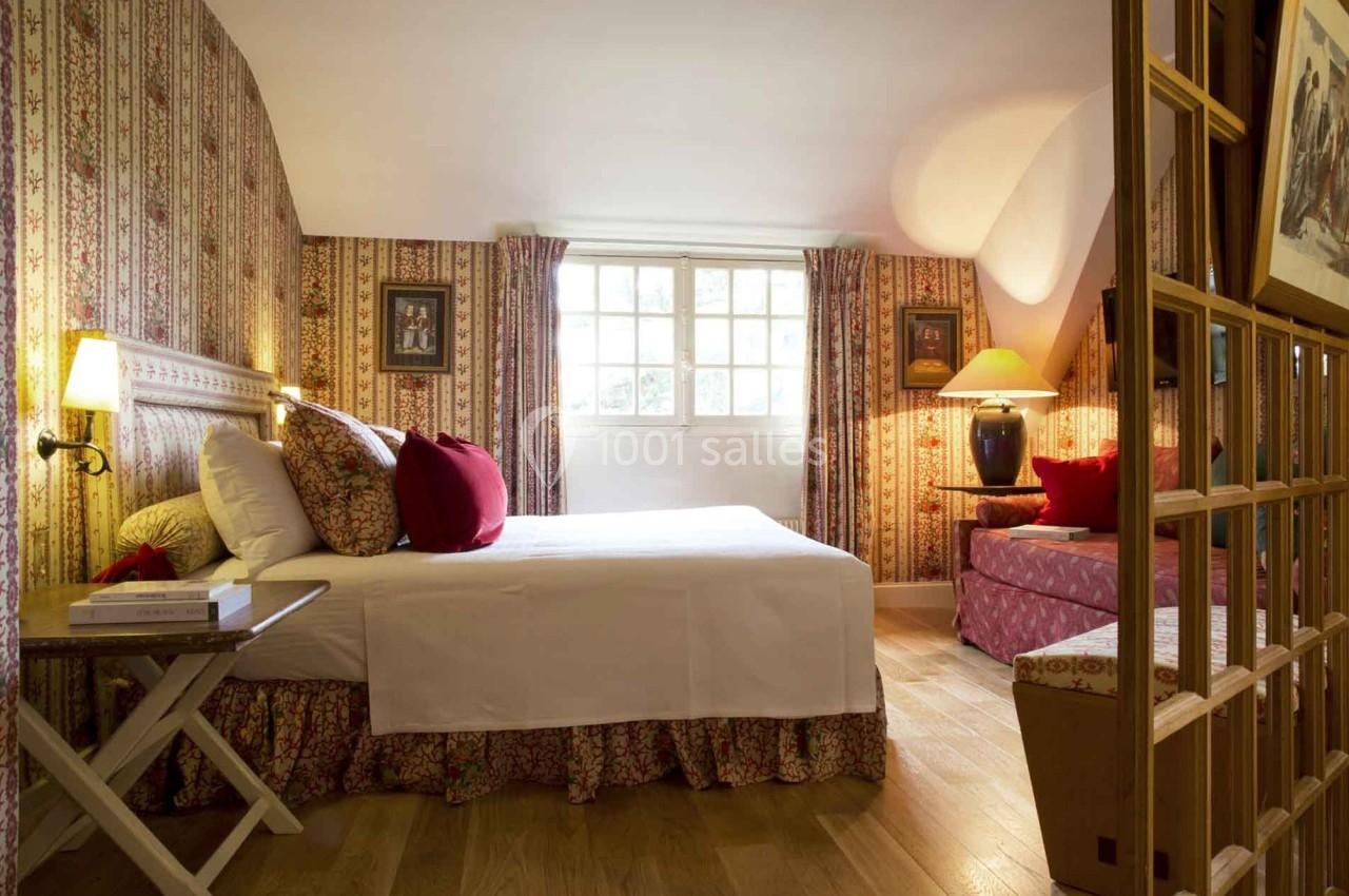 Chambre avec lit double, décorée de motifs floraux, éclairée par une fenêtre et des lampes, parquet au sol.