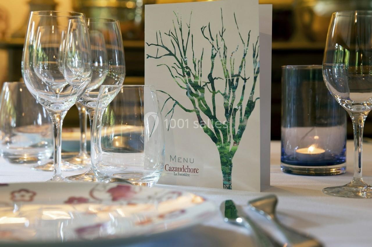 Table dressée avec des verres à pied, une assiette décorée et un menu illustré d'un arbre, éclairée par une bougie.