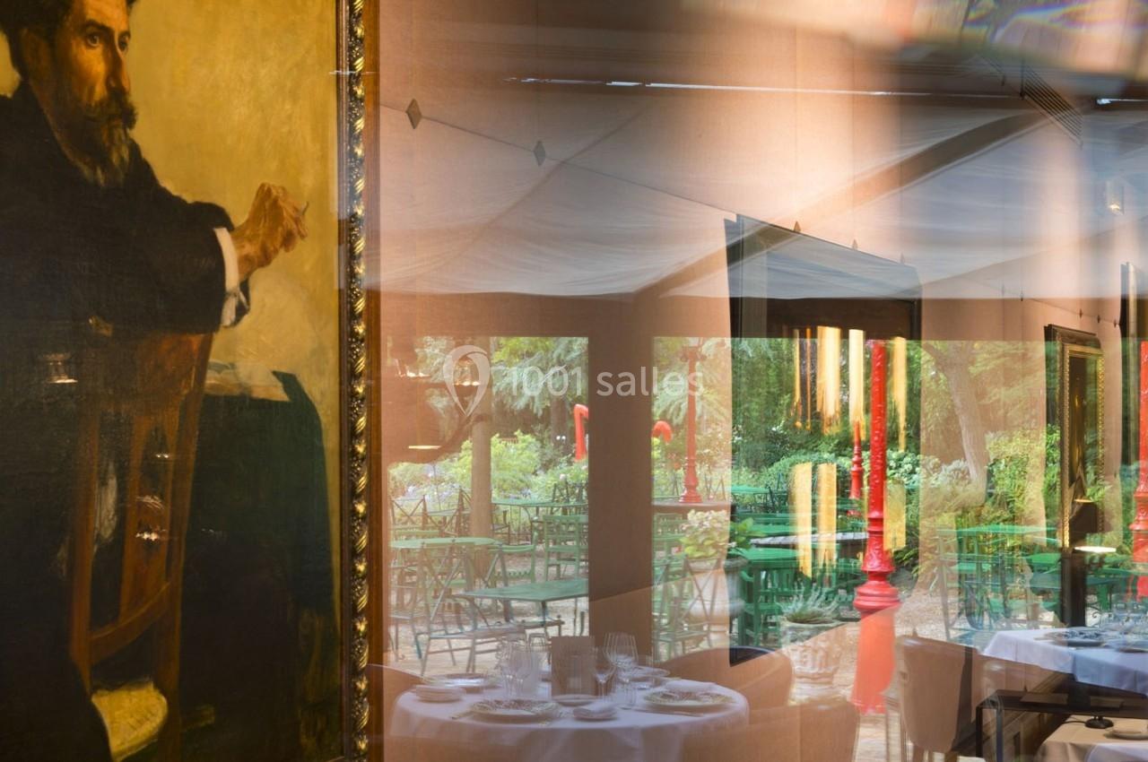 Reflet d'une salle de restaurant avec des tables dressées, mêlé à un tableau encadré dans une vitre.