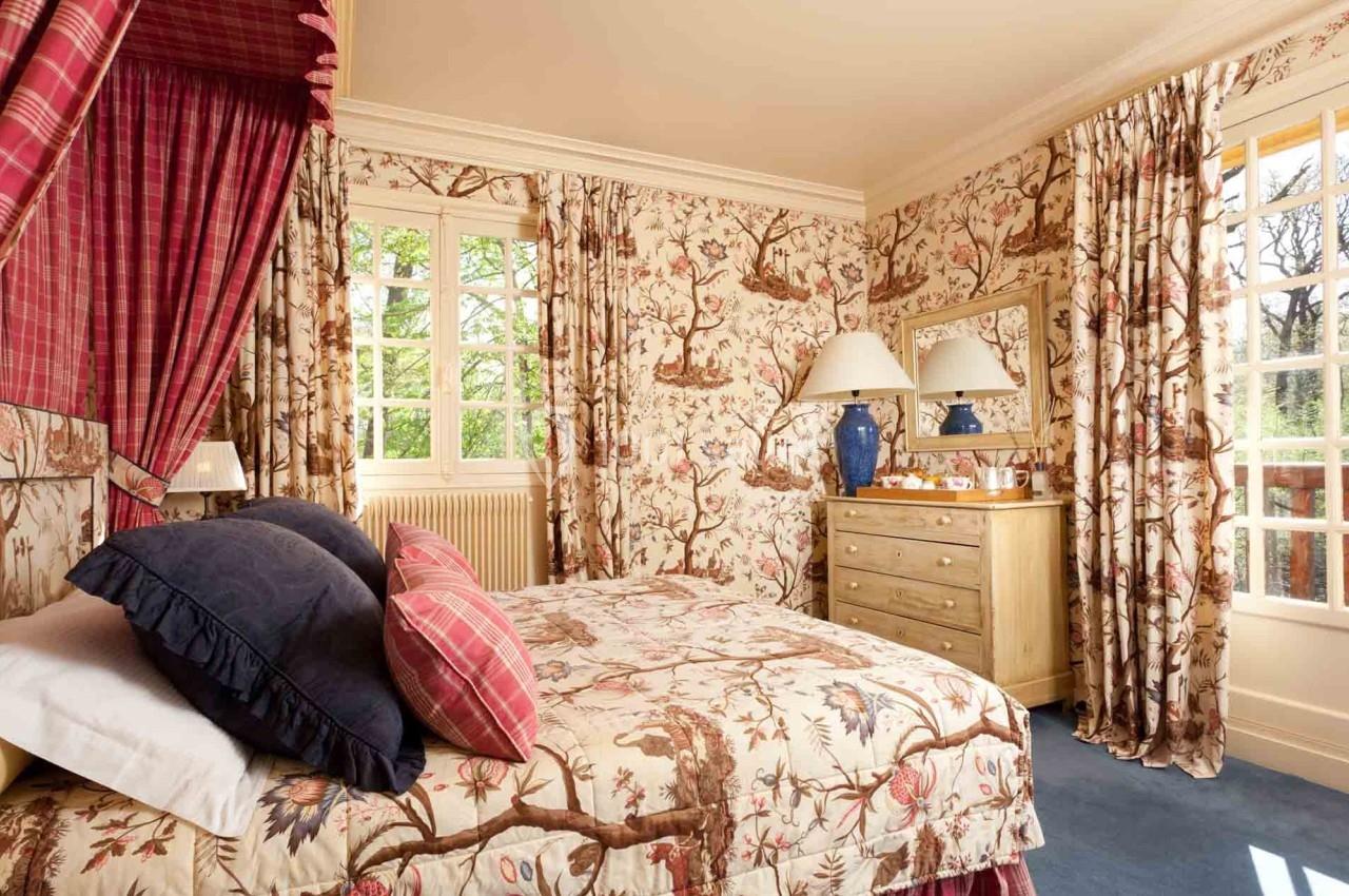 Chambre décorée avec des motifs floraux sur les murs, les rideaux et le lit, éclairée par une grande fenêtre.