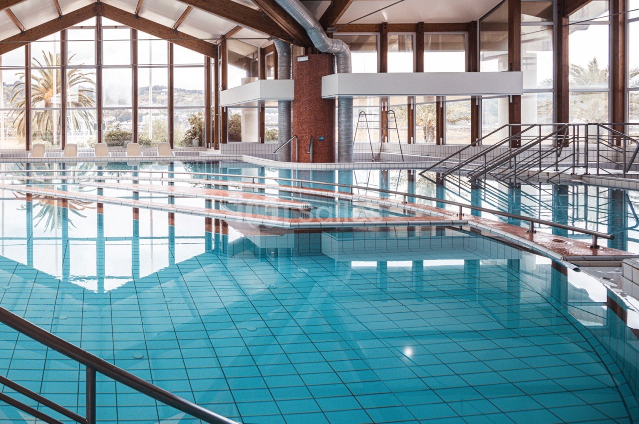 Piscine intérieure avec eau claire, rampes d'accès et grandes baies vitrées laissant entrer la lumière naturelle.