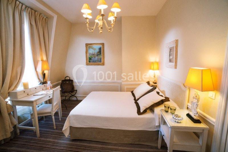 Chambre lumineuse avec un lit double, des meubles blancs, des lampes de chevet et un bureau près d'une fenêtre avec rideaux.