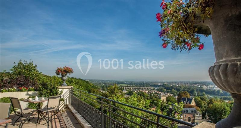 Terrasse avec table et chaises offrant une vue panoramique sur une vallée verdoyante et un ciel dégagé.