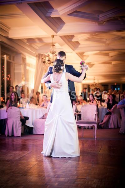 Un couple danse dans une salle de réception élégante, entouré d'invités assis à des tables décorées.
