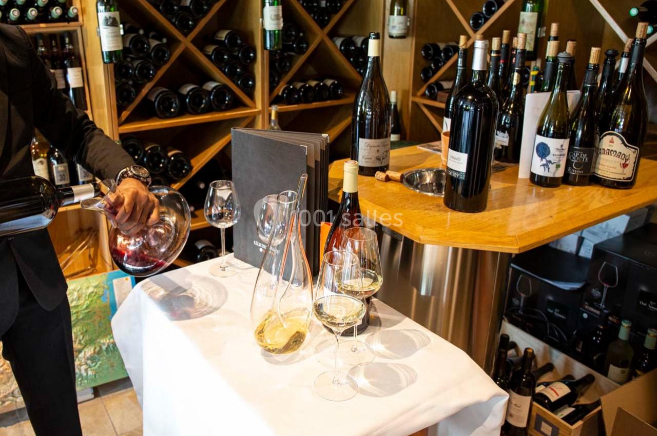 Un sommelier verse du vin rouge dans une carafe sur une table dressée avec des verres et des bouteilles de vin.