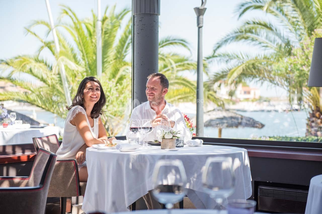 Un couple déjeune à une table élégante avec vue sur des palmiers et un paysage côtier ensoleillé.