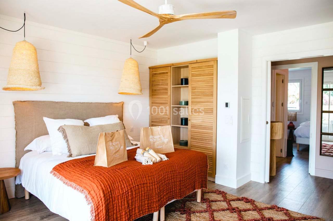Chambre lumineuse avec lit double, couvre-lit orange, lampes suspendues en osier et armoire en bois clair.