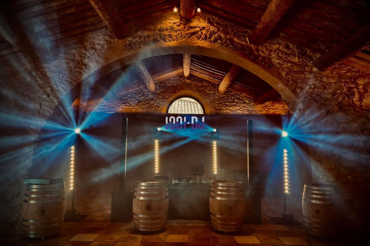 Salle voûtée en pierre avec éclairage coloré, barriques en bois et équipement de sonorisation au centre.