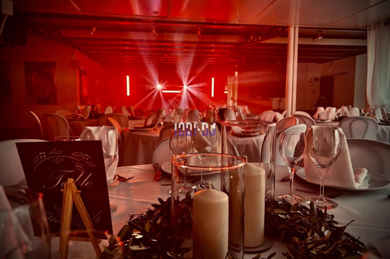 Salle de réception décorée avec des tables dressées, bougies et guirlandes, éclairée par des lumières rouges.