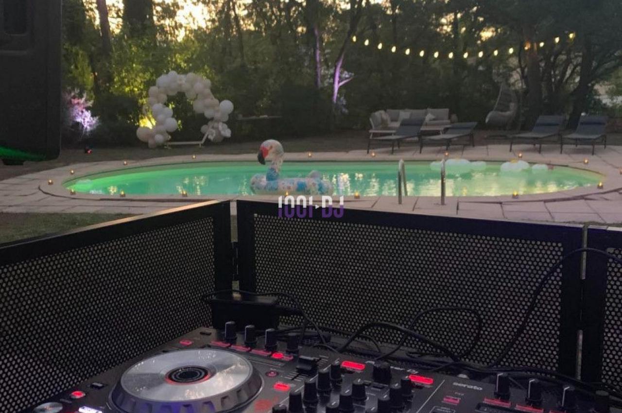 Table de mixage éclairée au premier plan, avec une piscine et un jardin en arrière-plan au crépuscule.