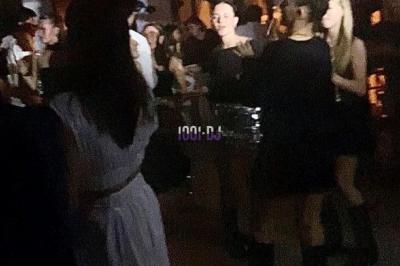 Personnes dans une ambiance tamisée, discutant et dansant près d'un bar décoré de fleurs suspendues.