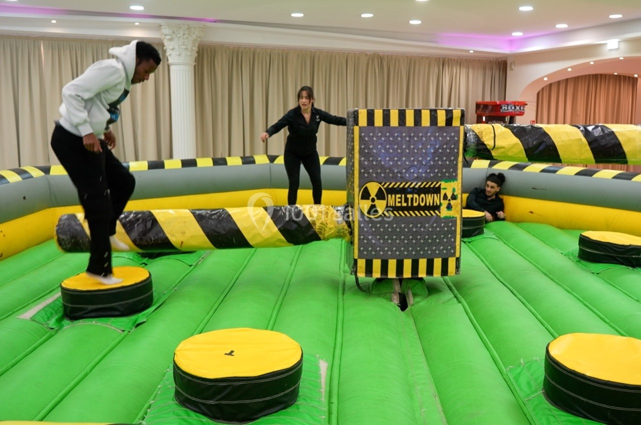 Personnes participant à un jeu d'obstacles gonflable avec une barre rotative à éviter dans une salle intérieure.
