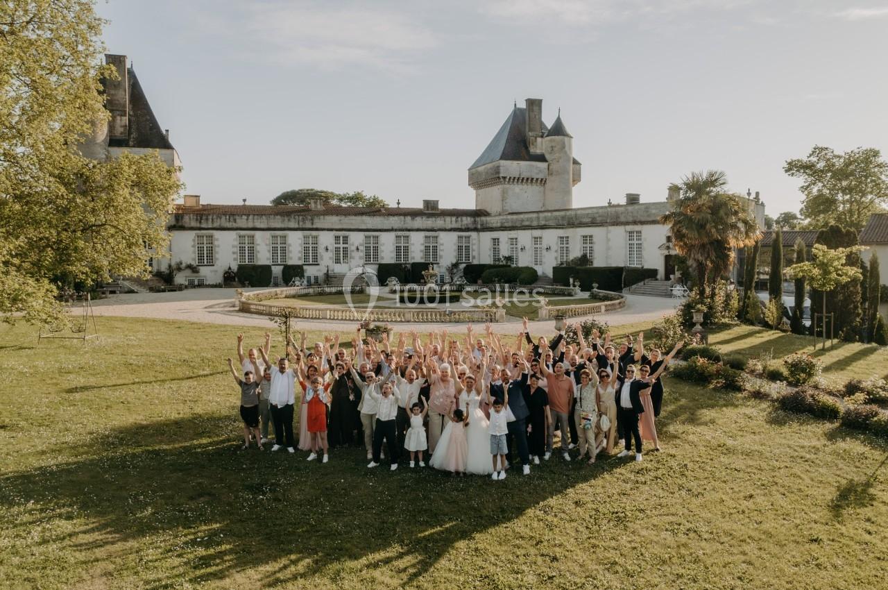Groupe de personnes célébrant un événement devant un château entouré de jardins sous un ciel clair.