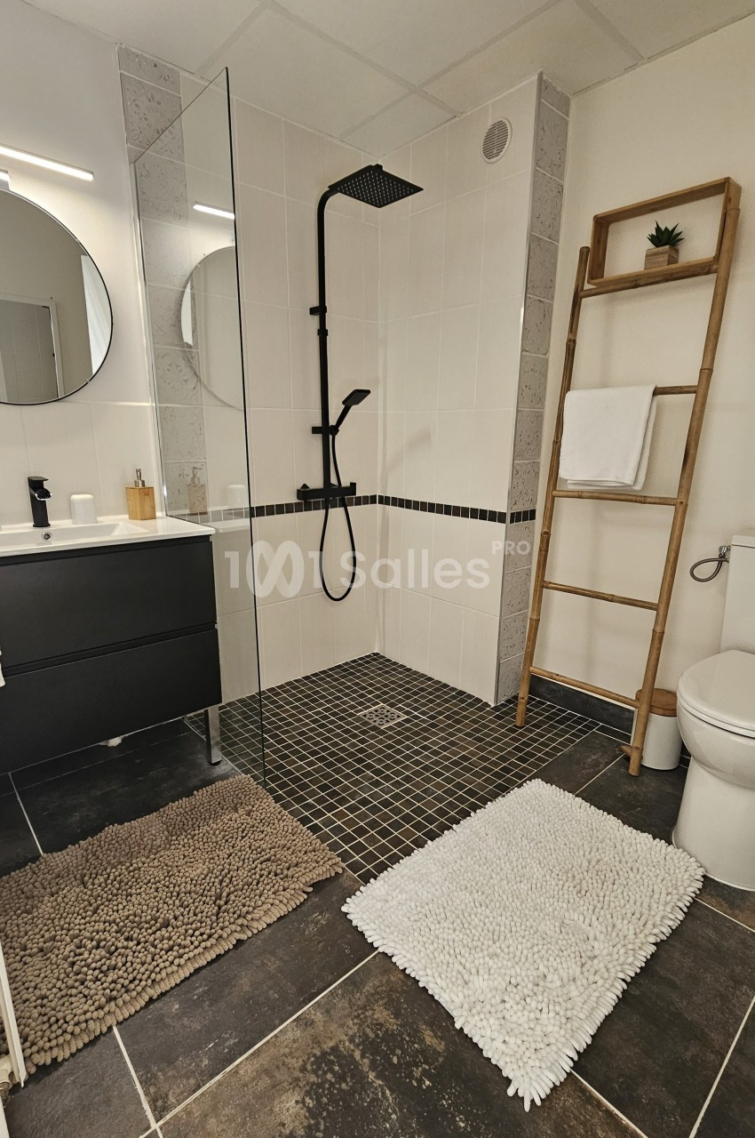 Salle de bain moderne avec douche à l'italienne, meuble noir, échelle porte-serviettes et tapis au sol.