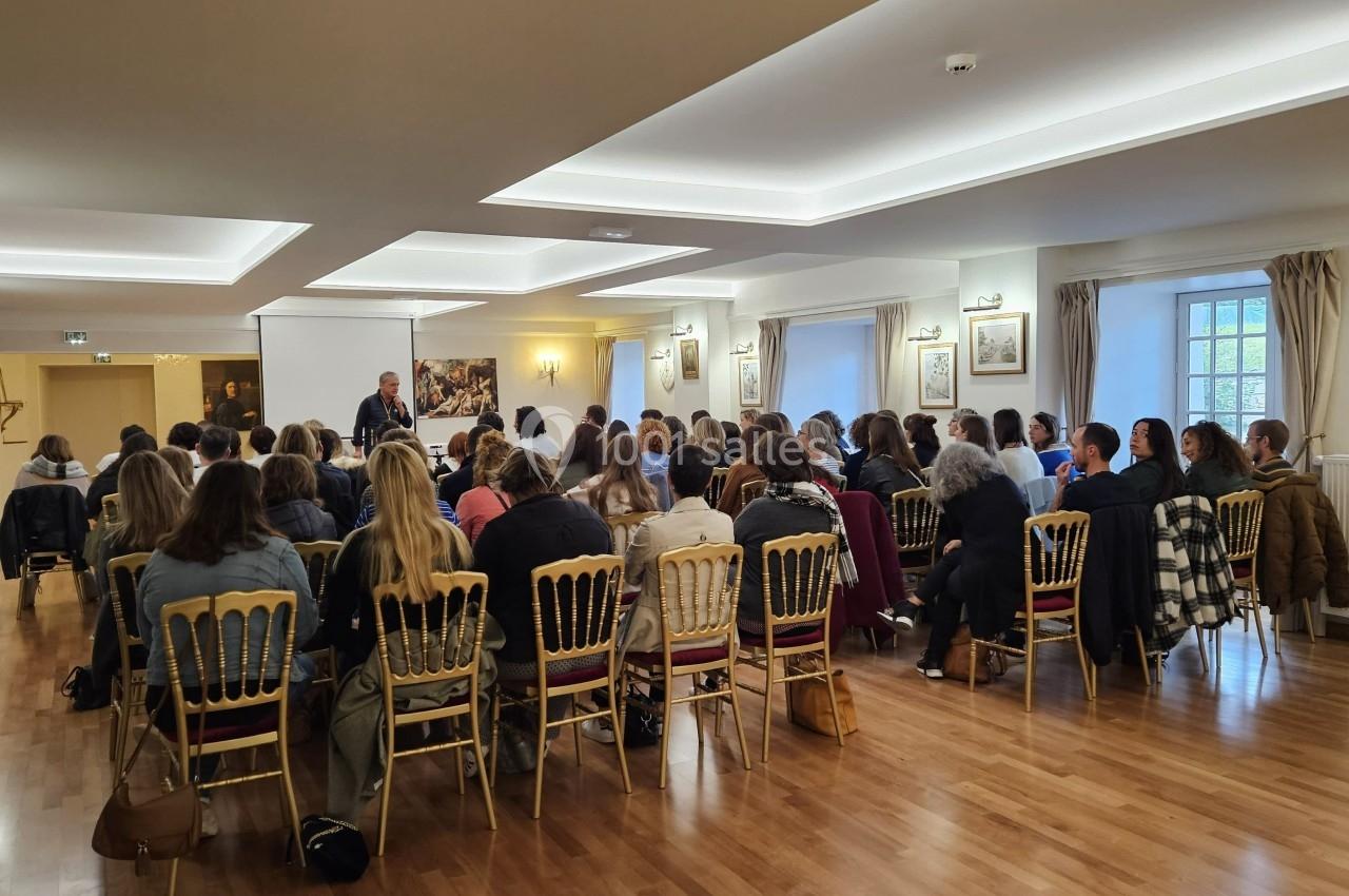 Un groupe de personnes assises dans une salle lumineuse, écoutant une présentation à l'avant.