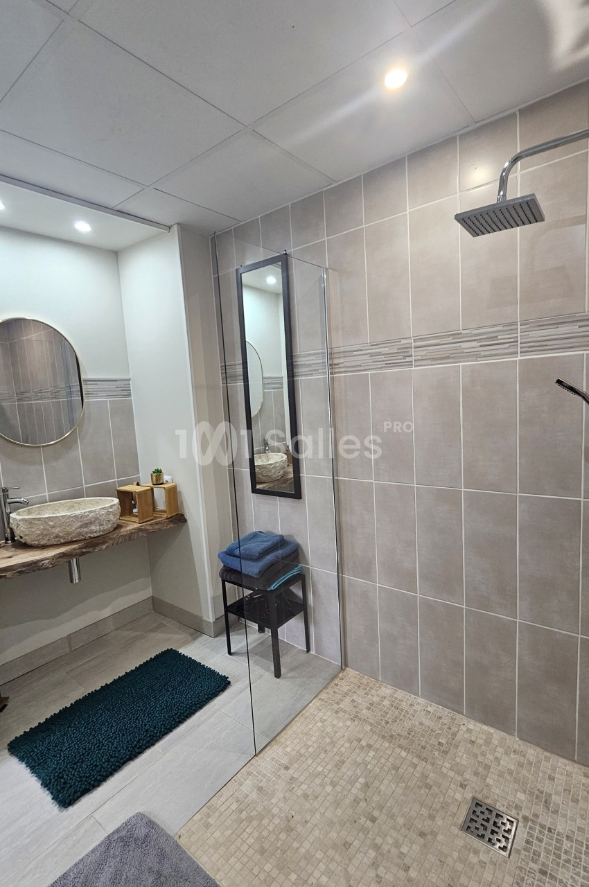 Salle de bain moderne avec douche à l'italienne, lavabo en pierre, miroir rond et éclairage encastré.