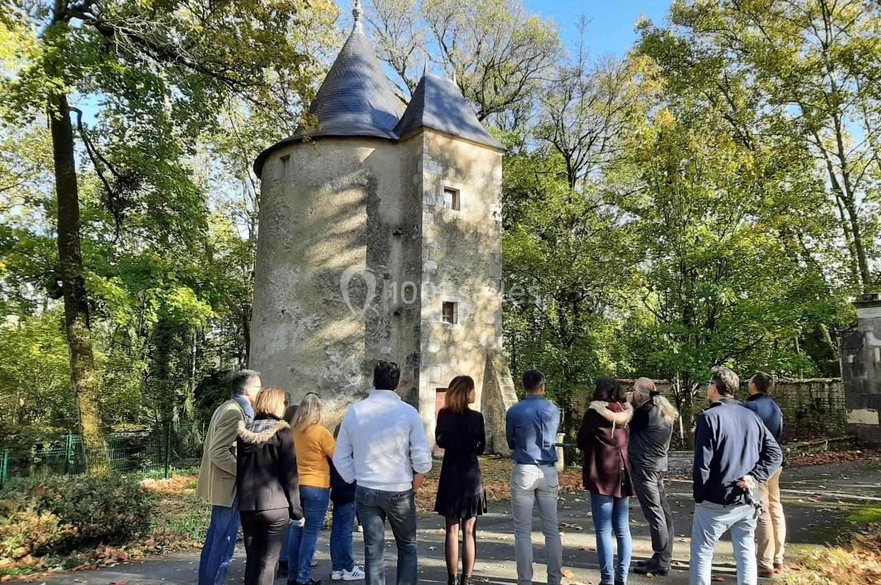 Un groupe de personnes observe une petite tour en pierre entourée d'arbres sous un ciel dégagé.