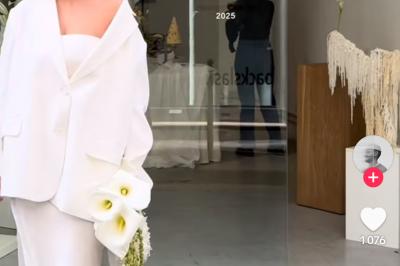 Une mariée en tailleur blanc tenant un bouquet devant une vitrine avec l'inscription ’Love Curated’.