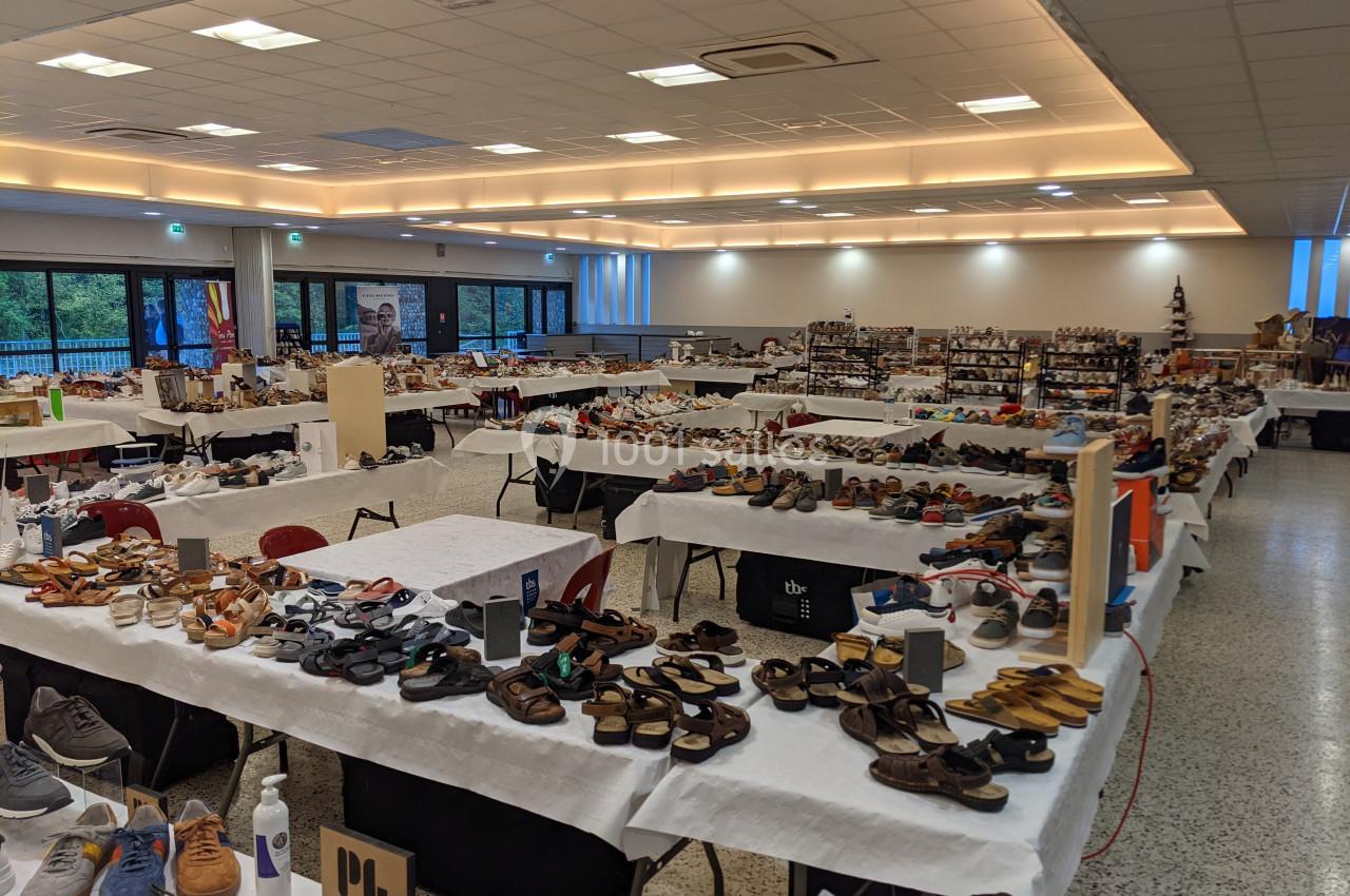 Salle d'exposition avec de nombreuses tables présentant des chaussures variées dans un espace lumineux.
