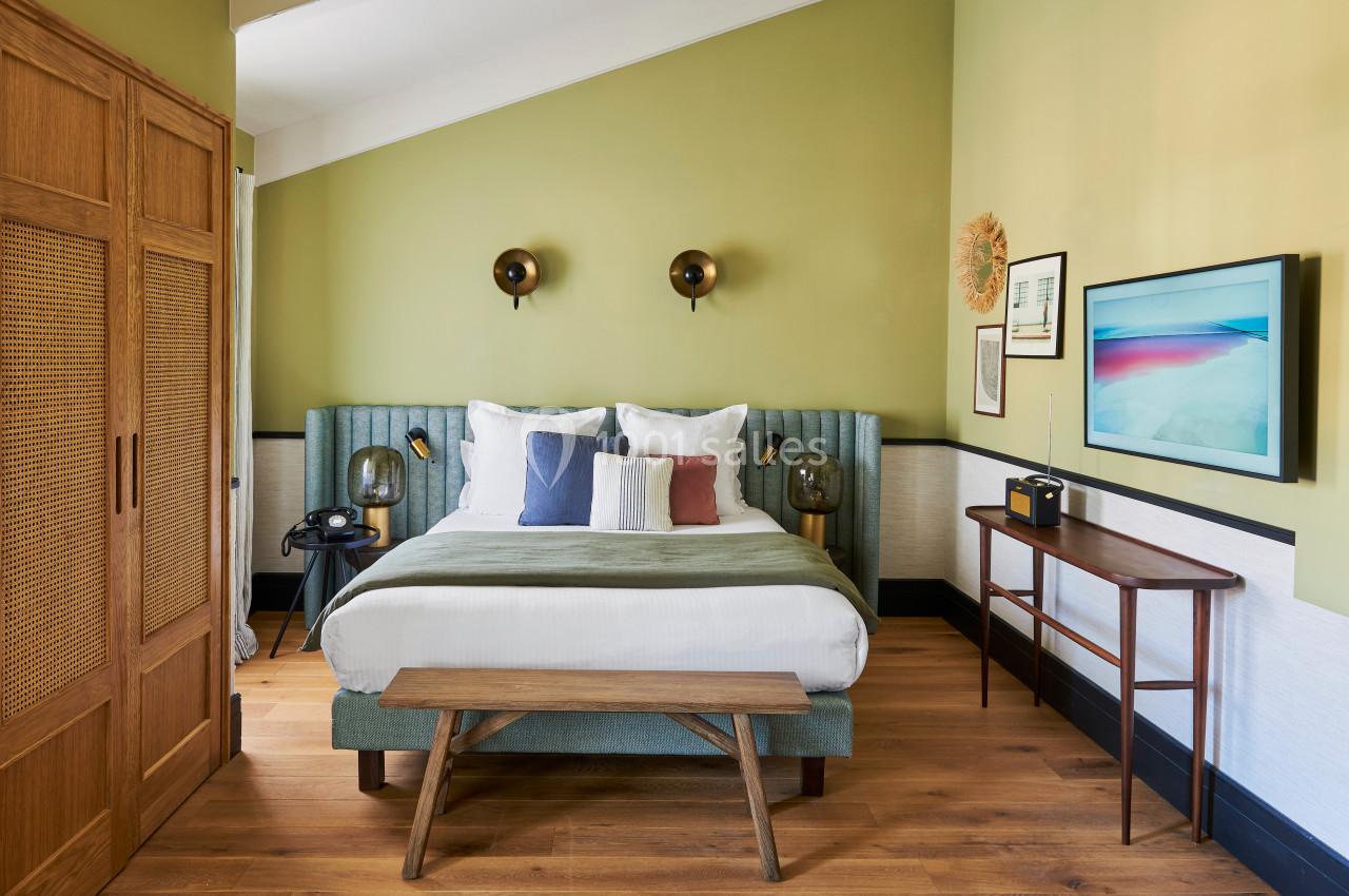 Chambre lumineuse avec lit double, murs verts, mobilier en bois et décorations murales modernes.